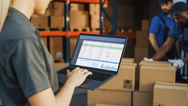 Warehouse Manager Using Laptop Computer To Check Inventory